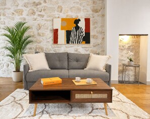 A living room with a grey sofa, a wooden coffee table with a Louis Vuitton box, a potted plant, and a stone wall. - 1550 Nazareth (Paris)