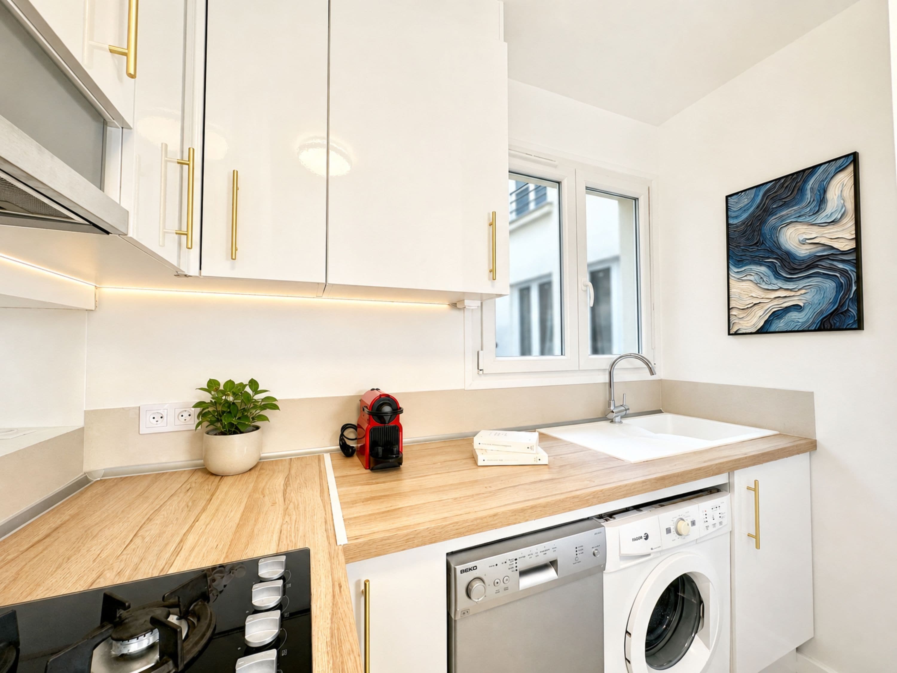 Una cocina moderna con armarios blancos, lavadora integrada, un lavabo y una ventana.