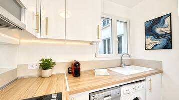 Una cocina moderna con armarios blancos, lavadora integrada, un lavabo y una ventana.