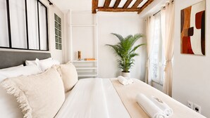 A bedroom with a bed, a potted plant, a painting, and a window with curtains. - 1550 Nazareth (Paris)