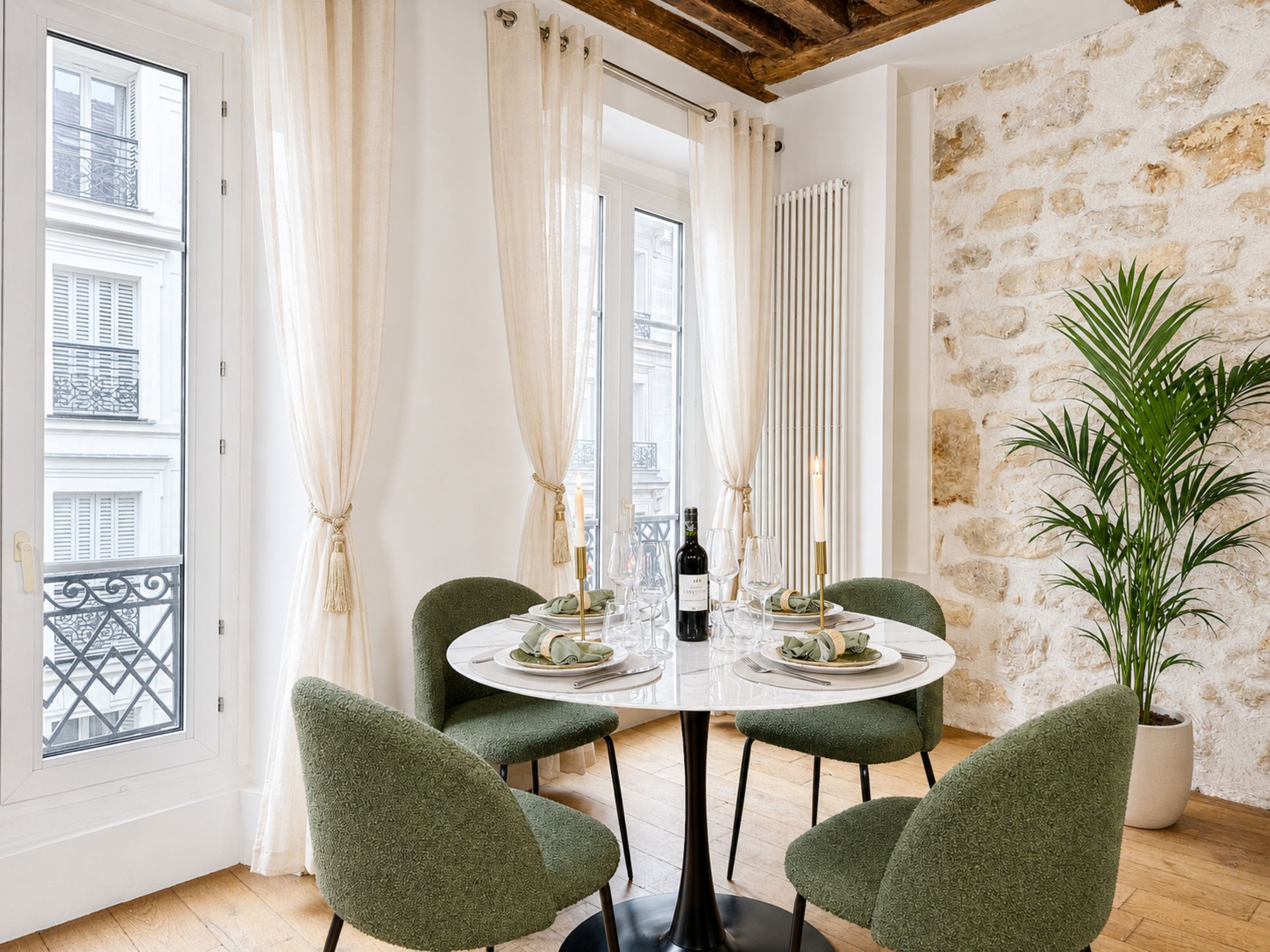 Un área de comedor con una mesa redonda, cuatro sillas, una planta en maceta y vistas de la ciudad a través de amplios ventanales.
