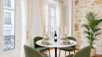 Un área de comedor con una mesa redonda, cuatro sillas, una planta en maceta y vistas de la ciudad a través de amplios ventanales.