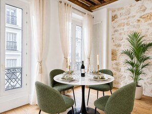 A dining area with a round table, four chairs, a potted plant, and a view of the city through large windows. - 1550 Nazareth (Paris)