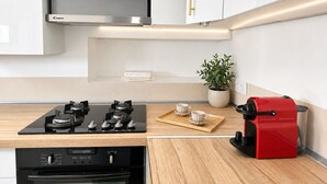 A modern kitchen with white cabinets, a stainless steel range hood, a gas stove, a red espresso machine, and a potted plant. - 1550 Nazareth (Paris)