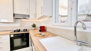 Una cocina moderna con gabinetes blancos, un extractor de acero inoxidable, horno empotrado, cafetera y una ventana sobre el fregadero.