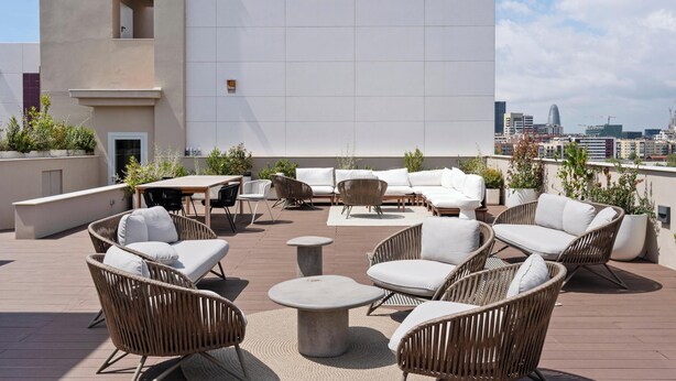 A rooftop terrace with wicker furniture, a round table, and a view of the city skyline.