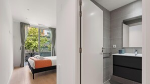 A modern bedroom with a bed, a balcony with curtains, and a bathroom with a sink and mirror.