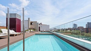 A rooftop pool with clear blue water, surrounded by lounge chairs and a city view.