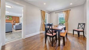 A dining area with a wooden table and chairs, a view of the kitchen, and a living room in the background. - Stay Roanoke | Cute 3BR Near Blue Ridge Parkway (Roanoke)