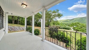 A covered porch with a view of a green landscape and a stone wall. - Stay Roanoke | Cute 3BR Near Blue Ridge Parkway (Roanoke)