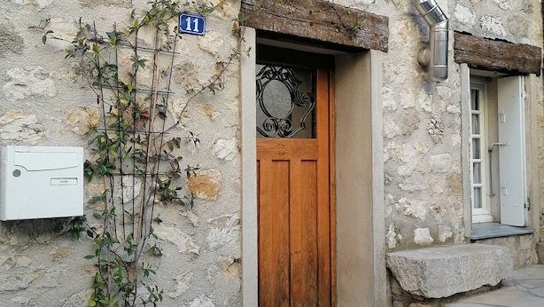 Un edificio de piedra con puerta de madera, una planta en maceta y un letrero azul con el número 11.