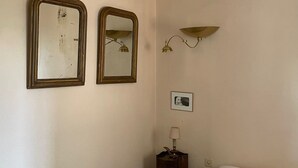 Un dormitorio con dos espejos en la pared, una lámpara de noche, una mesita auxiliar pequeña y una cama con almohadas.