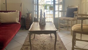 Una sala de estar con un sofá rojo, una mesa de centro de madera, una lámpara, una silla y vistas a un área exterior con plantas y un edificio.