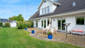 Een huis met een overdekte veranda, tuinmeubilair buiten en een kleine schuur.