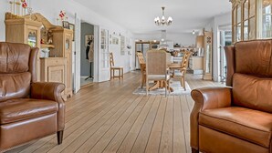 Een ruime woonkamer met leren banken, een eethoek met houten stoelen, en een keuken op de achtergrond.