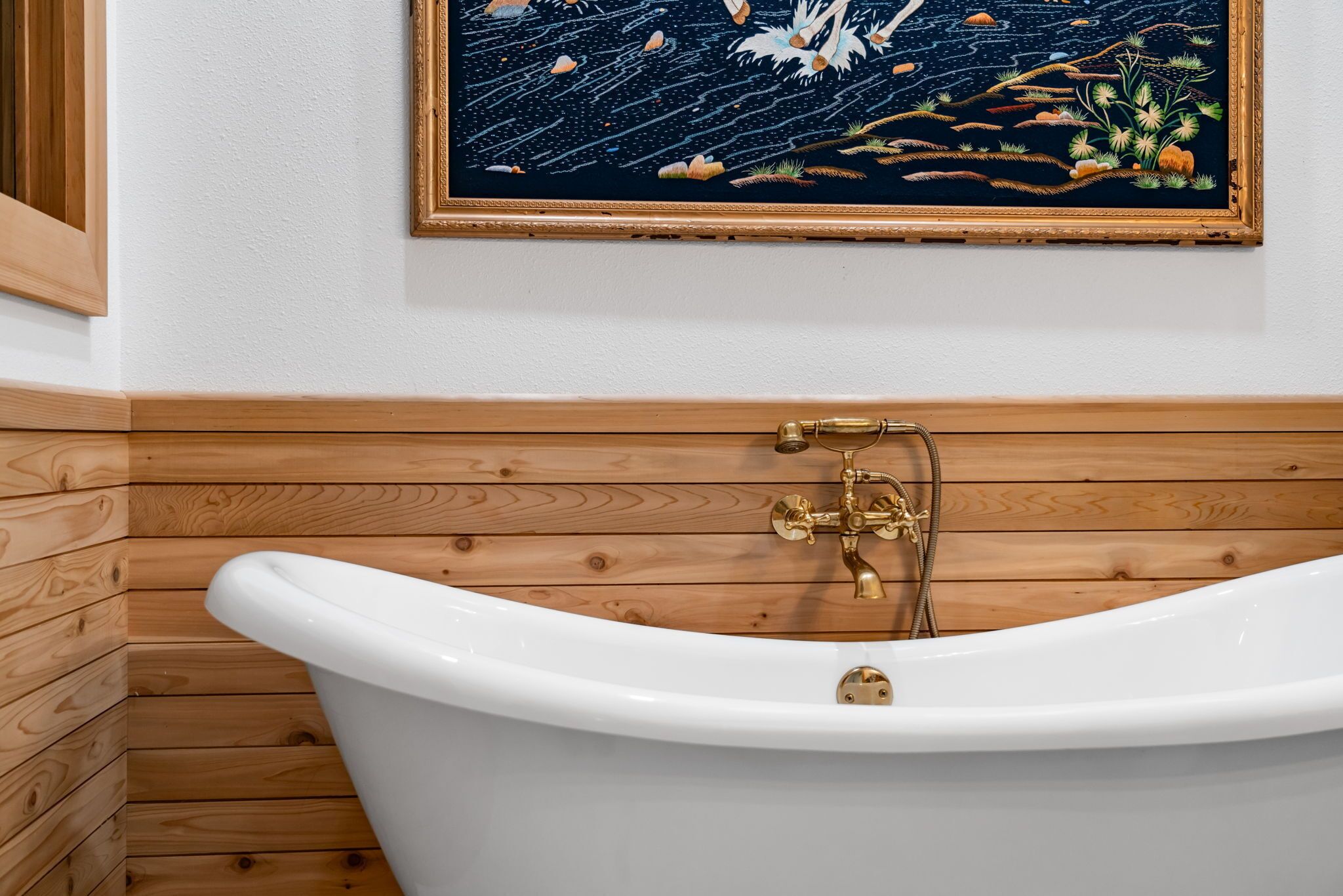 A white bathtub with brass fixtures in a wooden-paneled bathroom.