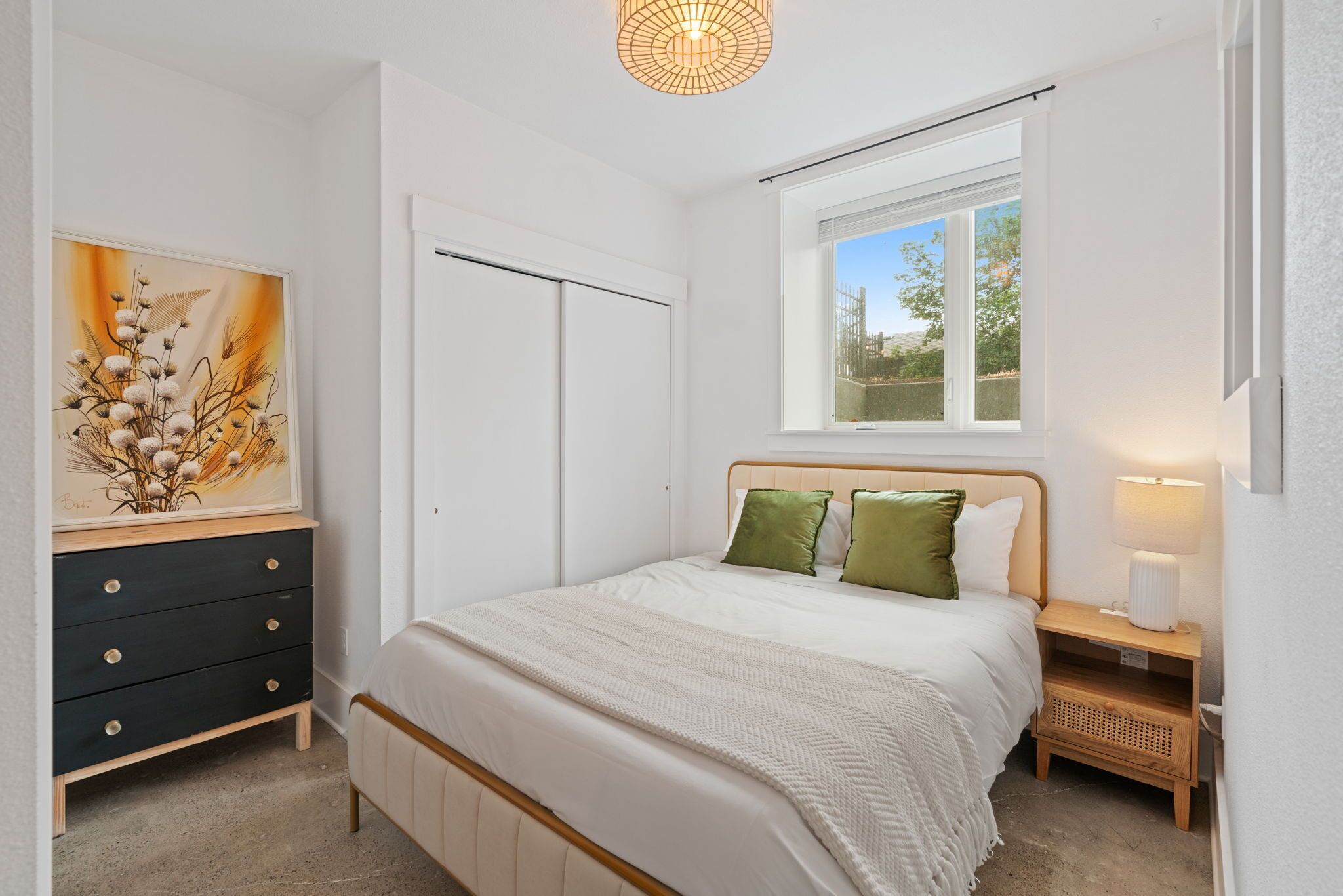 Une chambre à coucher avec un lit, une table de chevet, une commode, une fenêtre et un tableau.