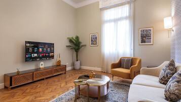 A living room with a flat-screen TV, a potted plant, a sofa, a coffee table, and a patterned rug.