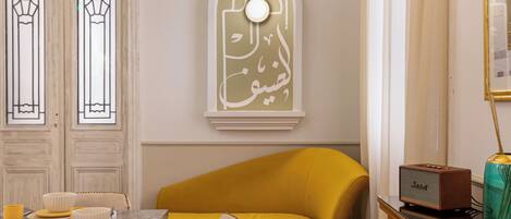 A dining area with a marble table, wooden chairs, a yellow sofa, and a patterned rug.