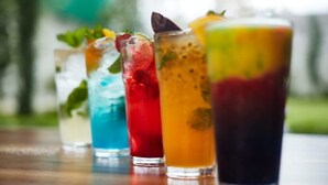 Four colorful drinks with ice cubes and garnishes on a wooden table. - Donix Suites  (Njoro)