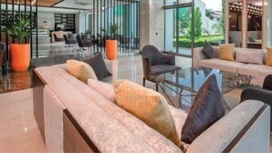 A modern lounge area with sofas and armchairs, a glass coffee table, and large windows offering a view of the outdoors. - Donix Suites  (Njoro)