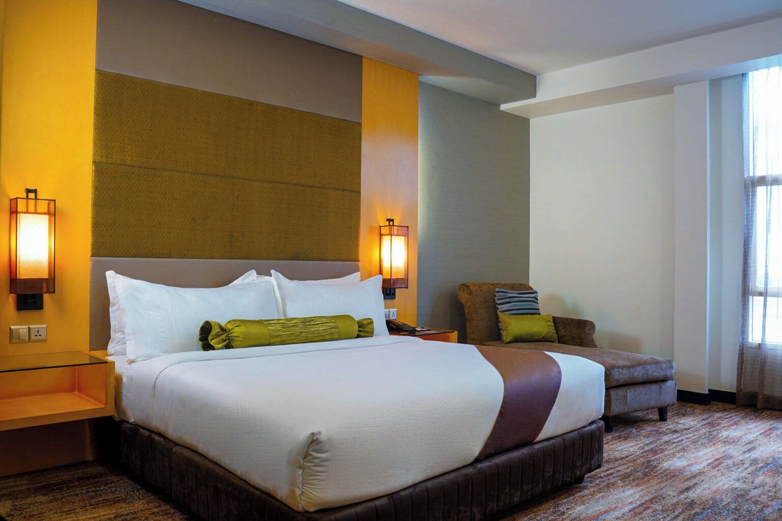 A hotel room with a large bed, two bedside tables, a chair, and a window with curtains.
