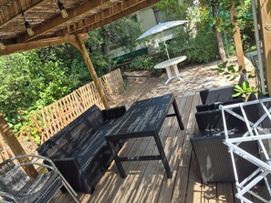 Eine Holzterrasse mit Gartenmöbeln, darunter ein Tisch und Stühle, umgeben von viel Grün.