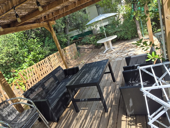 A wooden deck with outdoor furniture, including a table and chairs, surrounded by greenery.