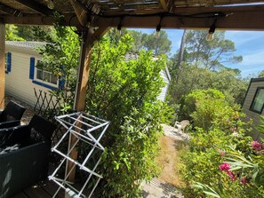 Un patio couvert aménagé avec du mobilier d’extérieur, un étagère en métal et une végétation luxuriante.