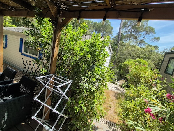 A covered patio area with outdoor furniture, a metal rack, and lush greenery.