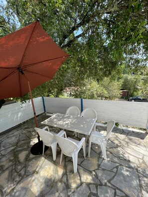 An outdoor patio with a table and chairs, a red umbrella, and a white fence.