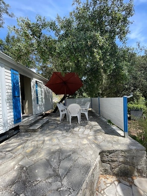Une terrasse avec un sol en pierre, une table et des chaises blanches, et un parasol rouge.