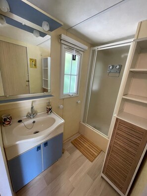 Ein Badezimmer mit Waschbecken, Spiegel, Fenster, Dusche und Holzschrank.