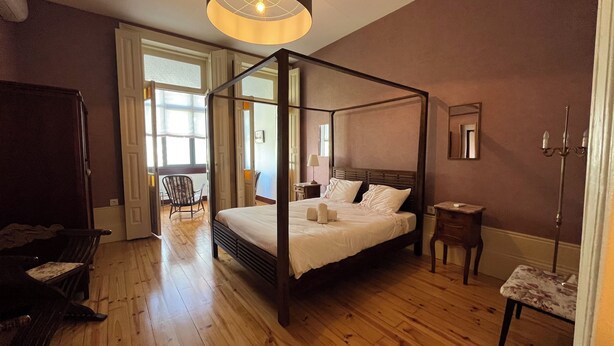 A four-poster bed in a room with wooden flooring, a chair, a bedside table, and a mirror on the wall. - Vila Camélia - Suite Namorados (Porto)
