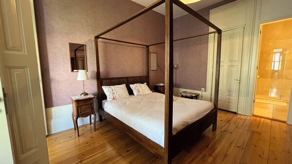 A four-poster bed with a nightstand, a mirror, and a door to a bathroom. - Vila Camélia - Suite Namorados (Porto)