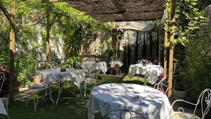 An outdoor patio with tables and chairs, surrounded by greenery and a pergola. - Vila Camélia - Suite Namorados (Porto)