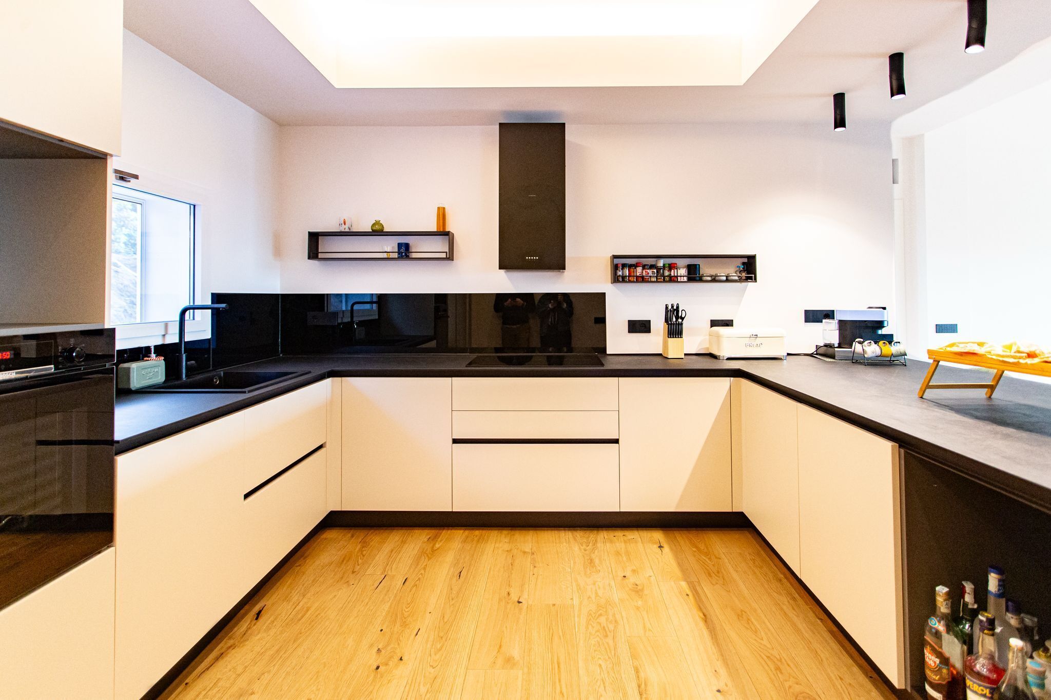 Una cocina moderna con armarios blancos, encimera negra y suelo de madera.