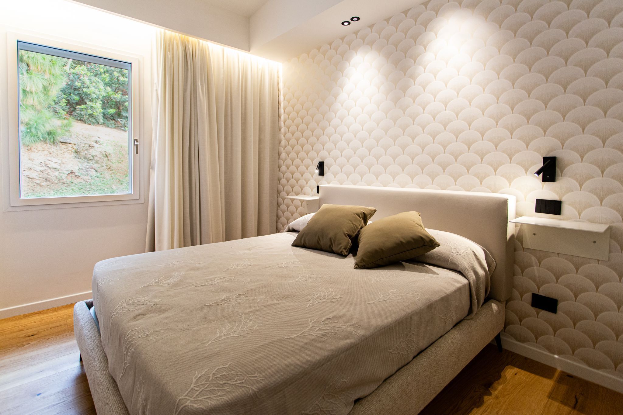 Une chambre avec un grand lit, une fenêtre avec des rideaux, un mur à motifs et une table de chevet avec une lampe.