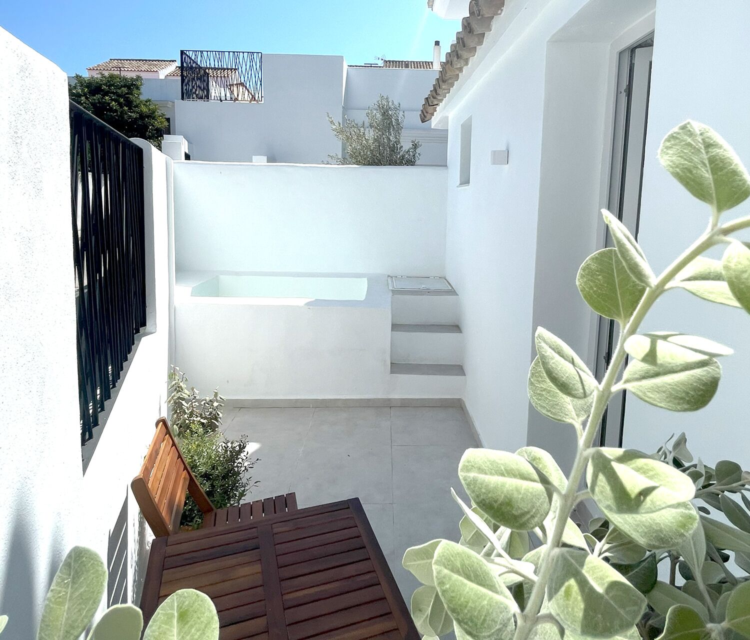 A narrow courtyard with a small pool, a wooden bench, and a potted plant.