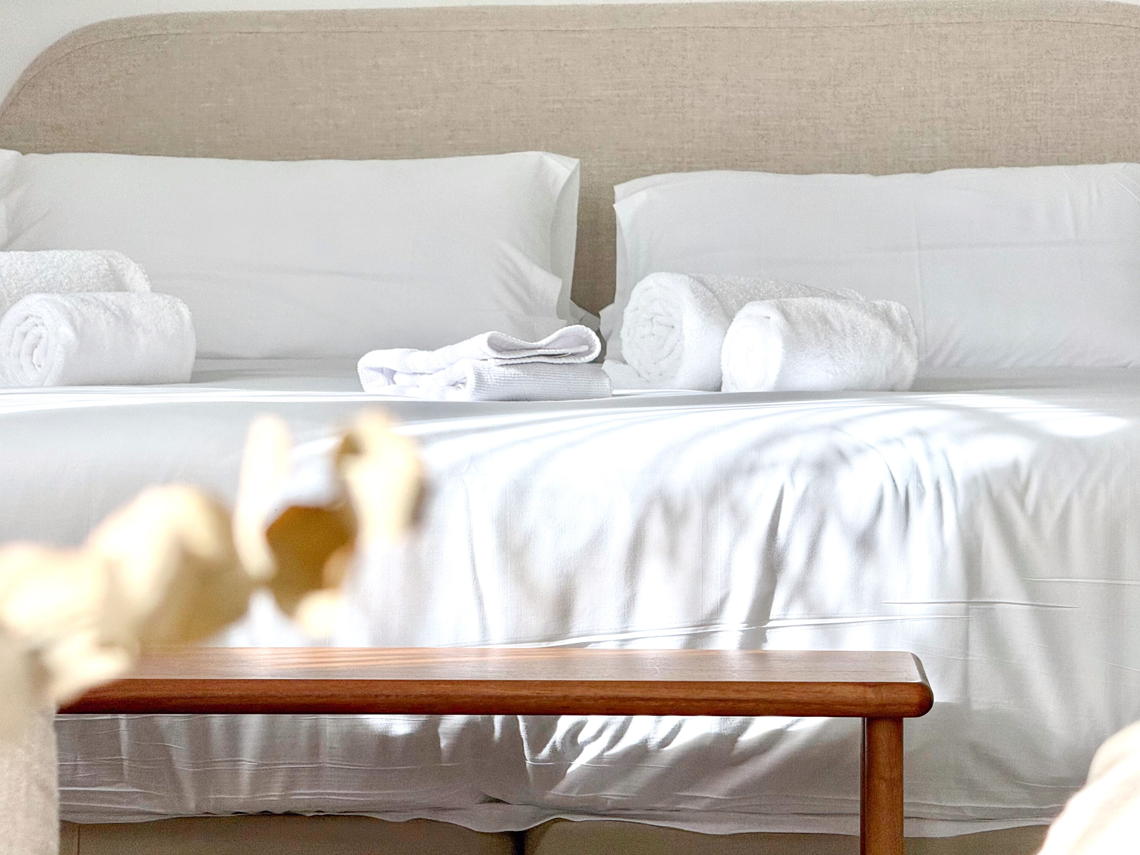 A hotel room with a bed, pillows, and a wooden bench.