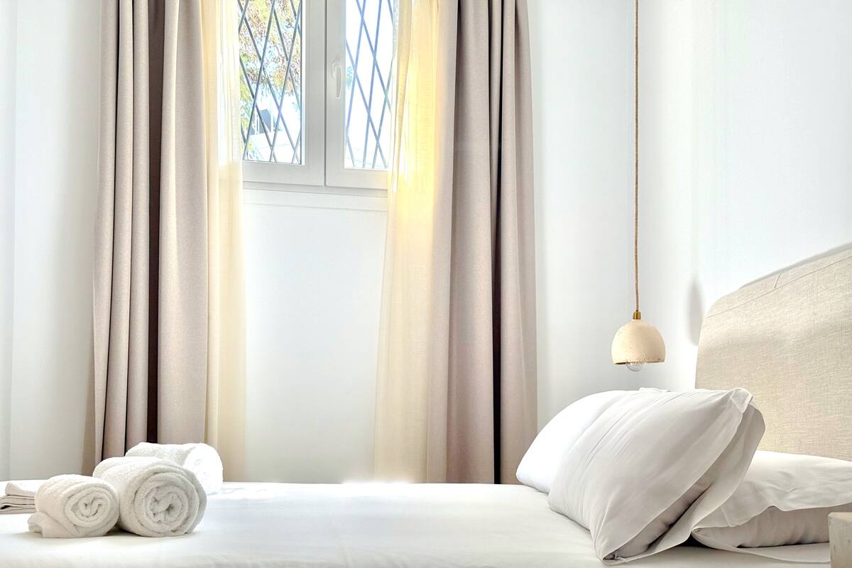A hotel room with a bed, curtains, a window, and a lamp.
