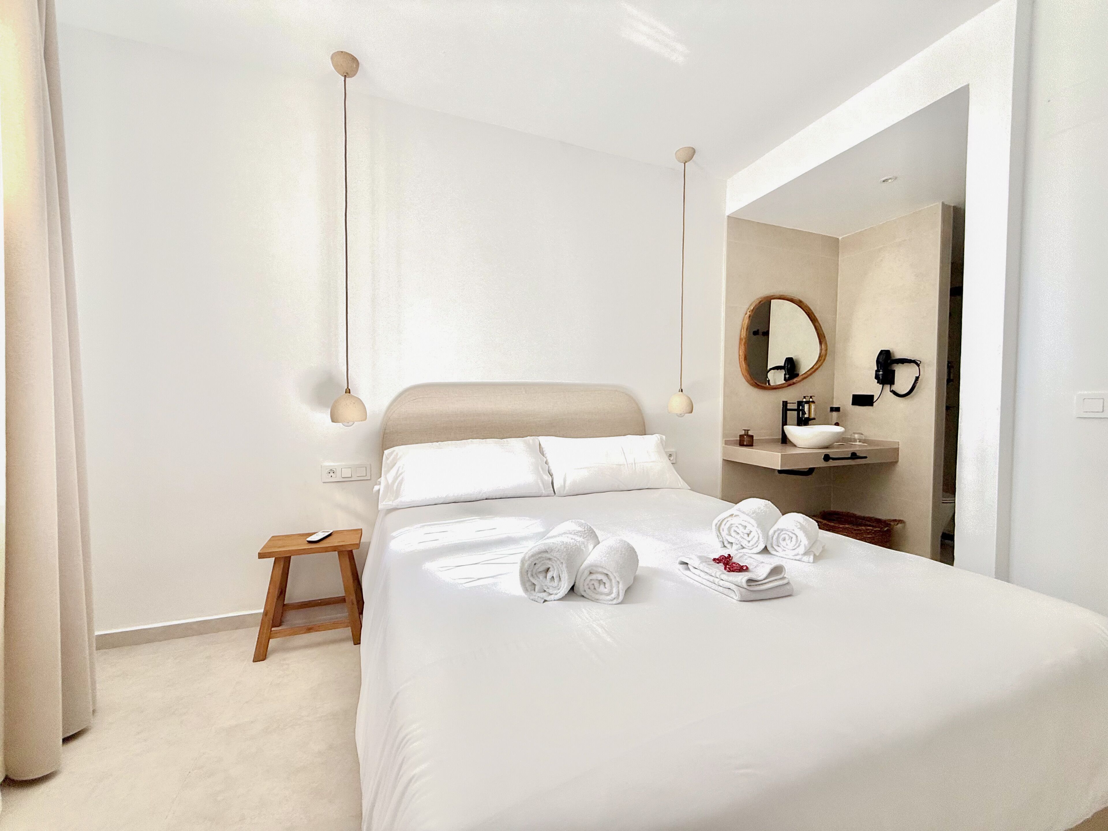 Quarto de hotel com cama, mesa de cabeceira e banheiro visível através de uma porta aberta.