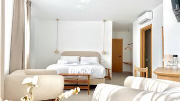 Una habitación de hotel moderna con una cama, dos sillones, una mesita y una puerta que da a otra habitación.