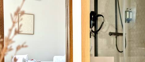 Habitación de hotel con cama, mesita de noche, unidad de aire acondicionado y zona de ducha con puerta de cristal.