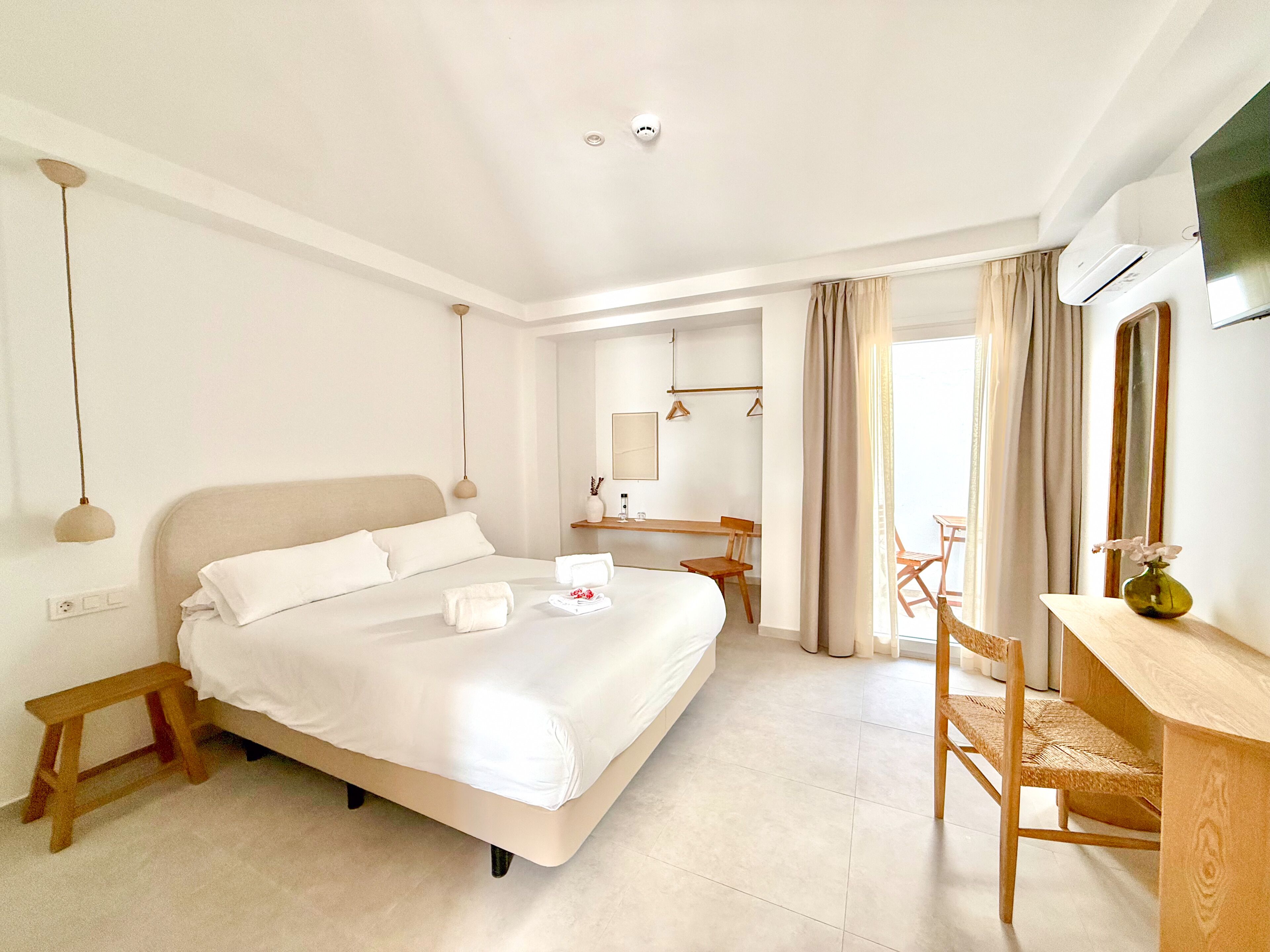 Habitación de hotel con cama, mesita de noche, silla, escritorio, espejo y aire acondicionado.