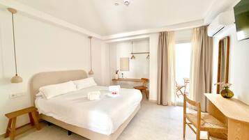 Habitación de hotel con cama, mesita de noche, silla, escritorio, espejo y aire acondicionado.