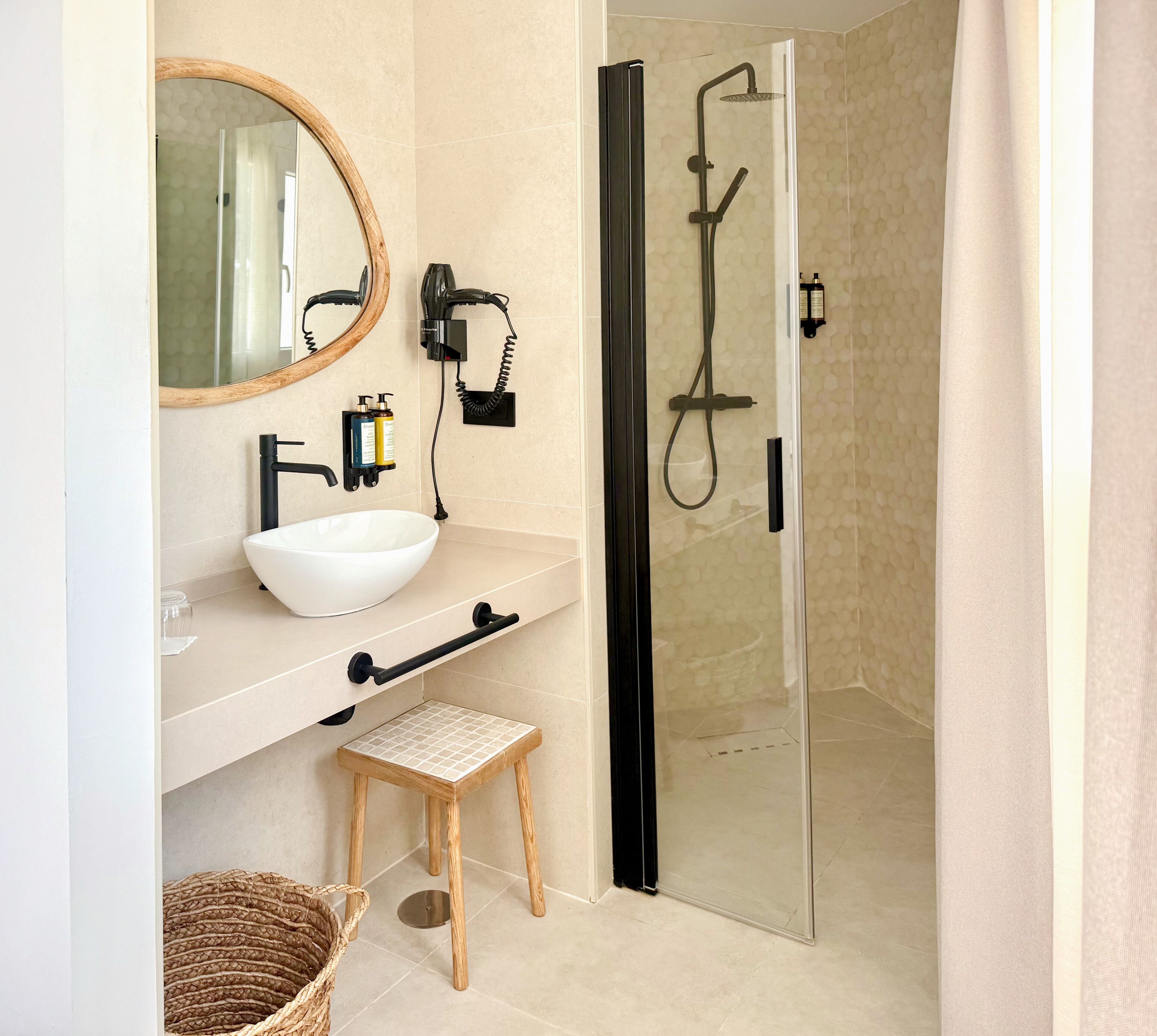 Un baño con lavamanos blanco, un espejo, ducha con puerta de cristal y un taburete pequeño.