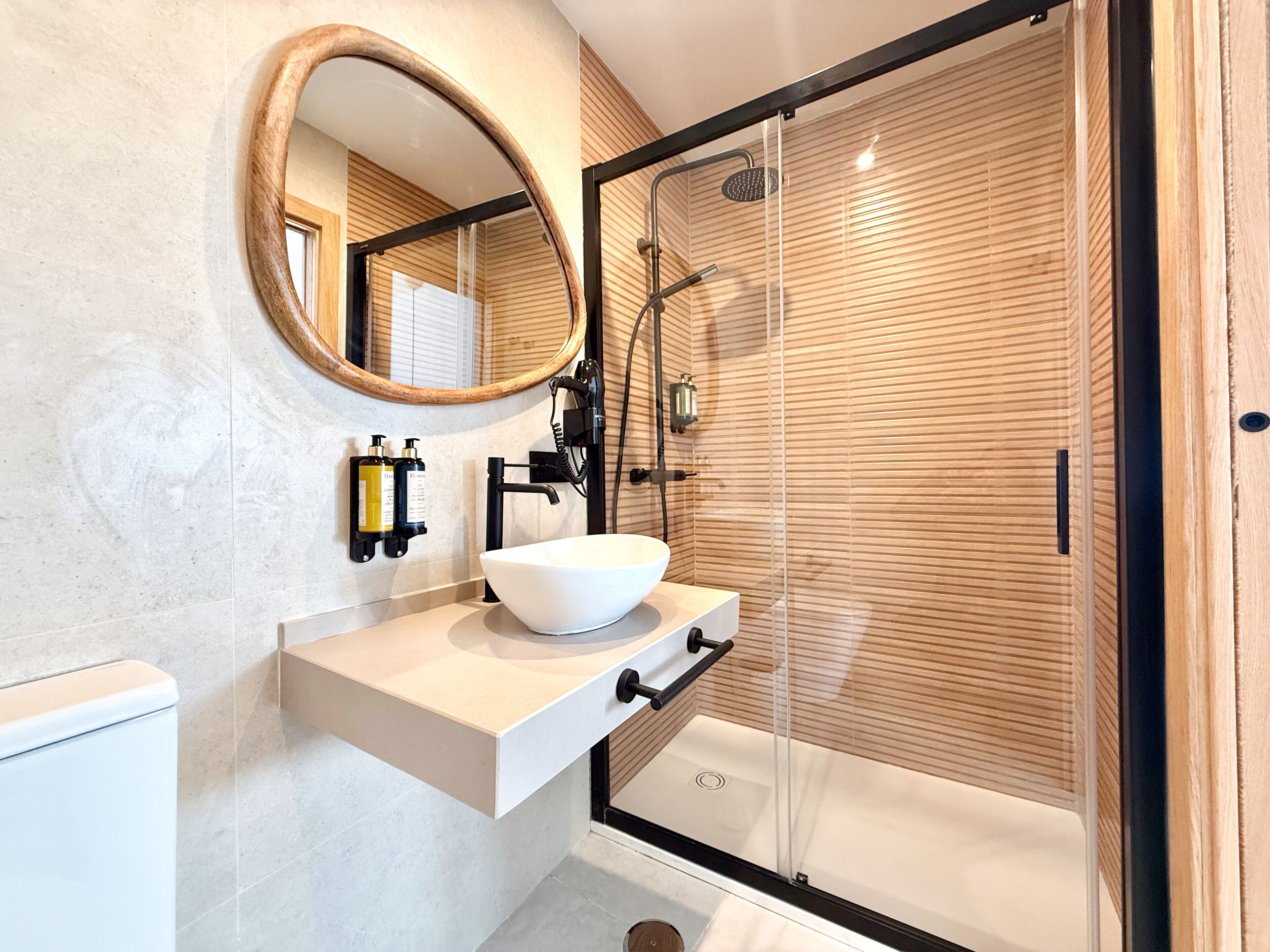 Un baño moderno con un lavamanos blanco, un espejo redondo y una cabina de ducha con paredes de vidrio.