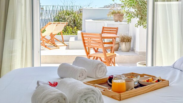 Een hotelkamer met een bed, een dienblad met ontbijtartikelen, een raam met uitzicht op een balkon en een tafel met stoelen.