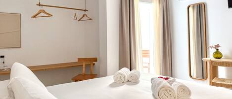 Habitación de hotel con cama, un banco de madera, perchero, espejo y ventana con cortinas.